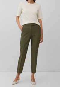 Dopasowane spodnie w kolorze oliwkowej zieleni z plisami, zestawione z kremową, teksturowaną bluzką. Charakteryzują się dopasowanym fasonem i subtelnym detalem z guzikami.