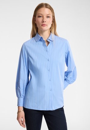 Camisa azul claro de botón con rayas verticales blancas, mangas largas abullonadas y un cuello clásico. Tejido suave con un ajuste estructurado.