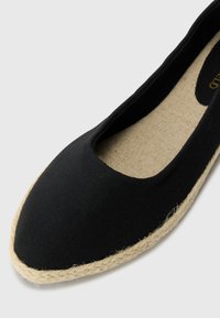 Sorte svart lerret flatt sko med rund tå og naturlig juta tau såle. Innvendig har den en teksturert beige såle.