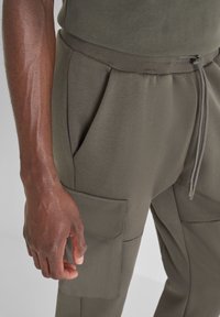 Olivgrüne Cargo-Hosen aus weichem Stoff, mit Falten, elastischem Bund, verstellbarem Kordelzug und mehreren Seitentaschen.