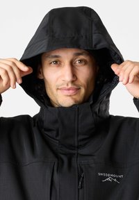 Schwarze wasserdichte Jacke mit hohem Kragen und verstellbarem Kapuze. Verfügt über eine mit Reißverschluss gesicherte Tasche und ein Logodetail auf der Brust. Glatte Textur.