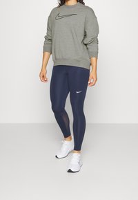Felpa grigia con logo Nike nero, abbinata a leggings blu navy con logo Nike bianco. Completata con scarpe da ginnastica bianche.