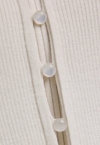 Rippstrick-beige Strickjacke mit weichem Griff, metallischen Fadenelementen und drei runden, durchsichtigen Knöpfen entlang der Knopfleiste.