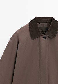 Cappotto marrone beige con colletto in corduroy, chiusura a un bottone e una texture liscia. Etichetta visibile all'interno del colletto.