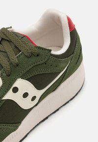 Olive green sneaker with suede and mesh materials, white accents, padded collar, and textured rubber sole. Red detail near the heel.