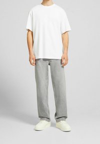 Camiseta blanca de algodón con un ajuste holgado, combinada con jeans de mezclilla gris claro y zapatillas blancas, mostrando un diseño casual y sencillo.