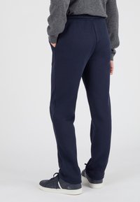 Pantalones de chándal azul marino hechos de tejido suave, con una cinturilla elástica y bolsillos laterales, combinados con zapatillas oscuras sobre un fondo neutro.