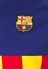 Blå och gul sportklädsel med den broderade FC Barcelona-logotypen, med röda och gula ränder i botten. Slät tygkvalitet.