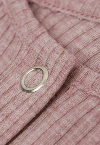 Różowa tkanina o fakturze z prążkowanym wzorem, z widocznym metalowym oczkiem blisko krawędzi. Zbliżenie pokazuje splot.