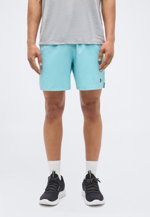 Άνδρας που φοράει γαλάζια αθλητικά σορτς, γκρι μπλουζάκι, λευκές αθλητικές κάλτσες και μαύρα παπούτσια τρεξίματος, στέκεται μπροστά από απλό φόντο.