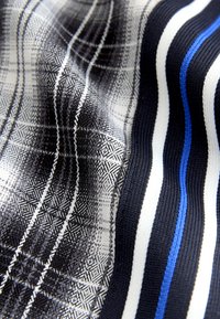 Tissu à carreaux noir et blanc avec rayures bleues et blanches, présentant un tissage texturé et une surface lisse. Des motifs géométriques subtils sont visibles.