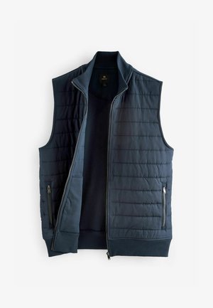 Marineblå polstret vest med høj krave, lynlås foran og sidelommer. Ribbet kant og subtil quiltet tekstur. Letvægtsstof.