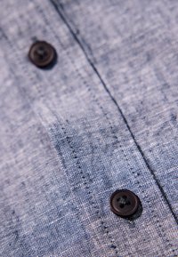 Tela azul claro con un tejido texturizado, que presenta dos botones oscuros y costuras visibles. Primer plano que muestra los detalles de la tela y la colocación de los botones.