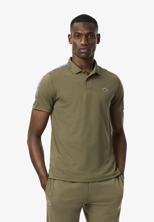 Olive green polo shirt made of cotton, featuring a two-button placket and a logo on the chest. Design includes patterned side accents.