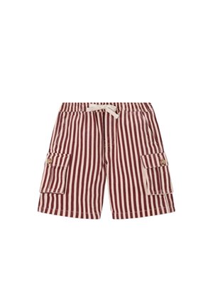 Garçon aux cheveux bouclés portant un t-shirt jaune, un short rayé rouge et blanc, des baskets, et portant un sac à dos vert à motifs sur une épaule.