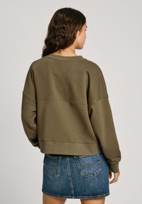 Sudadera corta de color verde oliva con hombros caídos, cuello de canalé y tejido texturizado; combinada con una minifalda de denim con bolsillos traseros.