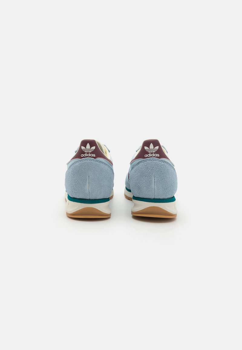 Zapatillas de ante azul con acentos en blanco y tono azul verdoso, con una pestaña trasera en marrón y suela blanca. Presenta el logo de Adidas en el talón y en la lengua.