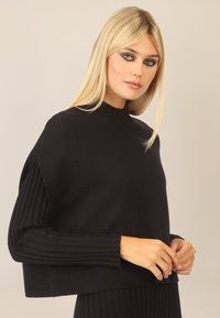 Maglione nero con colletto alto, maniche lunghe a coste e texture morbida. Presenta una vestibilità ampia e un design minimalista.