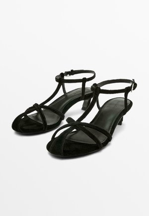 Sandales noires à talon bas avec des fines brides en velours qui se croisent sur les orteils et se ferment autour de la cheville avec de petites boucles.