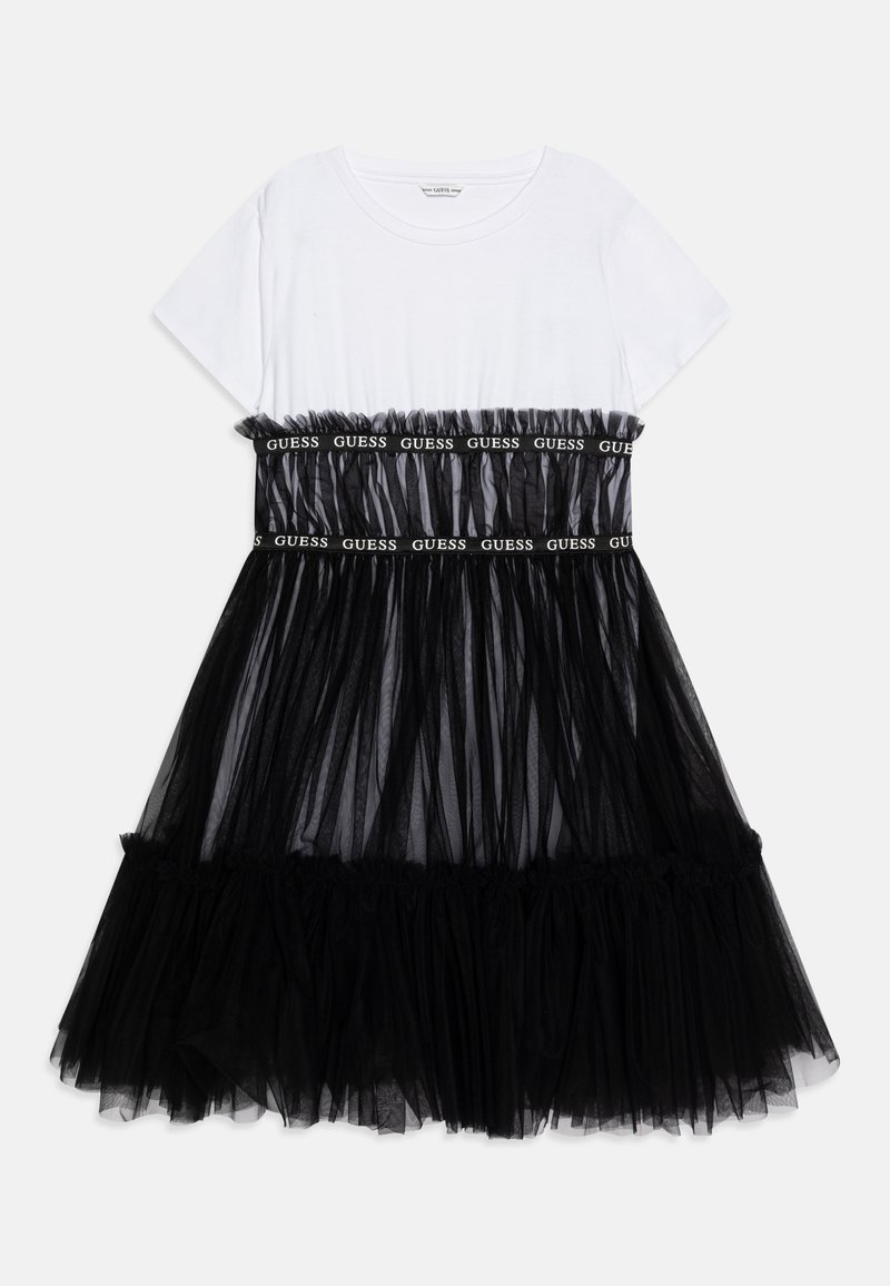 Robe blanche à manches courtes avec jupe en tulle noir superposée et deux bandes noires avec texte blanc "GUESS" sur la poitrine et la taille.