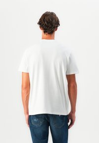 T-shirt en coton blanc avec un col rond et des manches courtes, présentant une coupe droite et une texture lisse. Porté avec un jean en denim bleu.