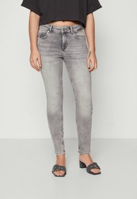 Grå skinny jeans med bleket vask, fem-lommers design, metallfester og en avslappet passform. Kombinert med svarte åpne tå hæler.