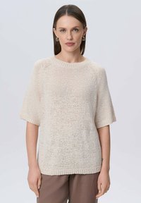 Sweter z krótkim rękawem w jasnym beżowym kolorze. Ma okrągły dekolt i luźny krój. Teksturowana tkanina o lekko otwartym splocie.