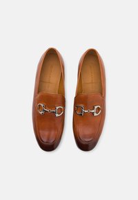 Mocasini din piele maro cu un design elegant, având accente de metal argintiu și o textură fină. Vârf rotunjit și branț căptușit.