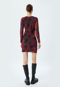 Langsleeve aansluitend jurkje in een rood- en zwart tie-dye patroon, gemaakt van stretchy stof. Gepaard met zwart kniehoge laarzen.