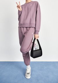 Lila sweatshirt och matchande joggers med vitt tryck, parat med en liten svart handväska och mönstrade sneakers. Mjuk tyg, avslappnad passform.