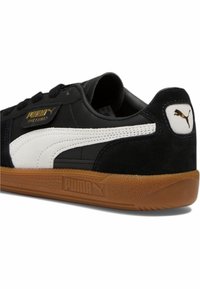 Čierne a biele tenisky z materiálov semiš a koža, s gumenou podrážkou, zlatým logom a bielym pruhom Puma.