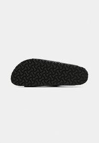 Semelle de chaussure noire avec un motif de semelle en vagues courbes répétées, présentée à plat sur un fond blanc.