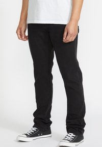 Jeans negri din denim cu o croială slim, având un design curat și cusături minime. Asortați cu adidași din pânză negri și albi.
