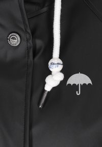 Melnā ūdensizturīgā jaka ar sudraba lietussarga grafiku, baltu auklu ar mezglu akcentu un sudraba pogu uz auduma.