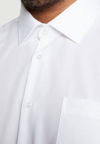 Witte overhemd met knopen, voorzien van een klassieke kraag, een gladde textuur en een enkele borstzak, met een strakke uitstraling en heldere plastic knopen.