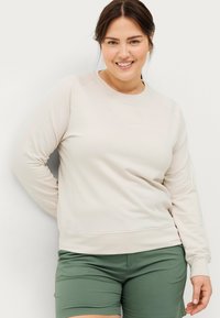 Lys beige sweatshirt med rund hals, der har et diskret præglogo, samlet med grønne shorts i en glat stof.