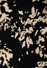 Tessuto nero con motivo floreale beige; presenta disegni intricati con forme e texture varie.