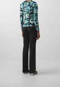 Dlouhý rukáv v modro-zeleném květinovém vzoru, spárovaný s černými kalhotami s vysokým pasem. Materiál vypadá hladce a má přiléhavý siluetu.