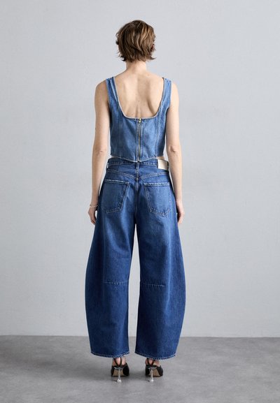 Denim kratki top s izrezom na leđima, uparen s farmerkama širokih nogavica. Oba komada su u srednje plavom pranju s minimalnim detaljima šivanja.