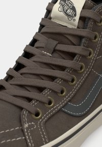 Brune semskede høje sneakers med grå accenter, cremefarvede snørebånd og metaløjer. Har hvid syning og et logo-patch på tungen.