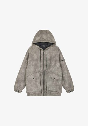 Giacca a vento grigia chiara con finitura testurizzata, due grandi tasche anteriori, zip nere e lacci. L'interno è foderato in nero.