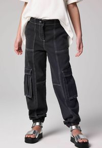 Musta cargo-housut valkoisilla ompeleilla, useilla taskuilla ja joustavilla lahkeilla. Yhdistetty kiiltäviin hopeisiin platform-sandaaleihin.