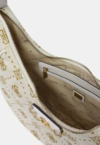 Sac à épaule en toile blanche avec un motif monogramme doré. L'intérieur est doté d'une doublure beige, d'une poche zippée et d'un détail de logo. Accents en métal doré.