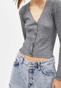 Grå ribbad stickad cardigan med V-ringning och sex bruna knappar, ihop med ljusblå högmidjade jeans.