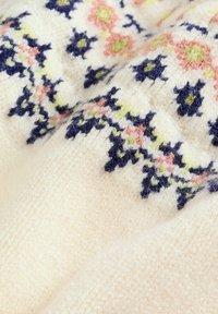 Strikket sweater med en cremet base og blomsterbroderi i pink, grøn og mørkeblå. Blød tekstur og synlige stikninger.