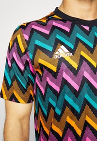 Kortärmad atletisk t-shirt med ett flerfärgat zick-zack-mönster i svart, rosa, orange, teal och gult mot en svart bakgrund.