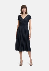 Robe bleu marine, longueur genou, avec des manches courtes et un décolleté en V. Corp de robe enroulé et jupe plissée, présentant une texture subtilement brillante.