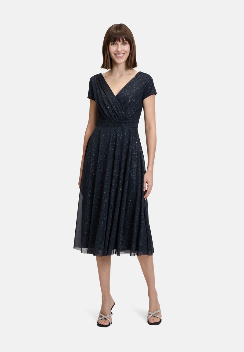 Robe bleu marine, longueur genou, avec des manches courtes et un décolleté en V. Corp de robe enroulé et jupe plissée, présentant une texture subtilement brillante.