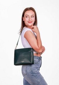 Zelená kožená kabelka přes rameno s minimalistickým designem, hladkou texturou, zapínáním na zip a nenápadným logem na přední straně.