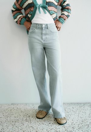 Person wearing light blue high-waisted jeans, beige moccasin shoes, white shirt, and a striped knit cardigan with teal, pink, and brown colors.